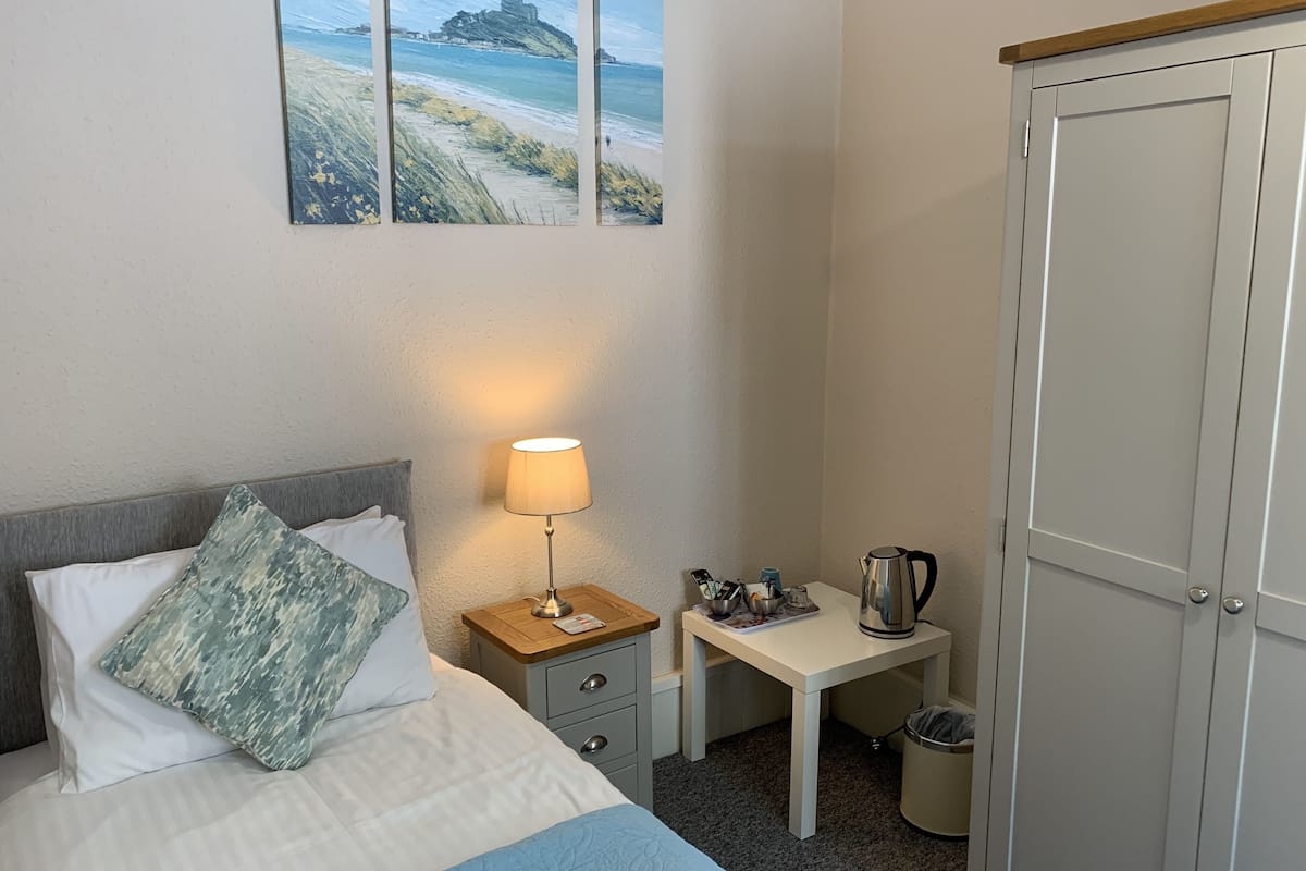A hotel room with a bed, a bedside table with a lamp, a small desk, and a wardrobe.