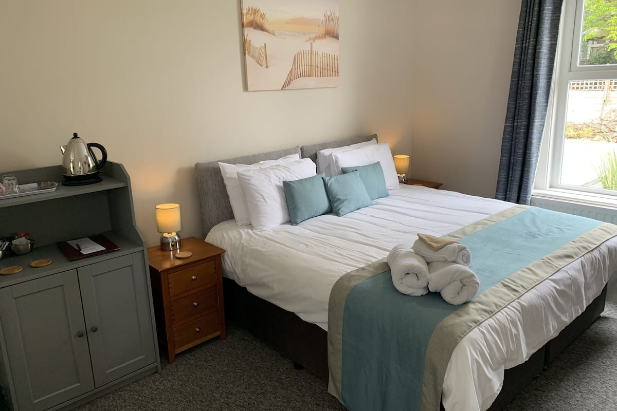 A neatly arranged hotel room with a bed, bedside tables, a small desk, and a window.