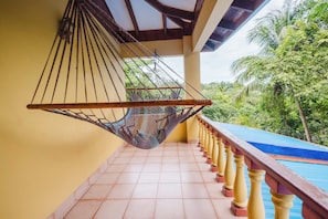 A hammock hanging from a balcony railing, with a view of a swimming pool and lush greenery in the background. - Hotel Las Tres Banderas (Quepos)