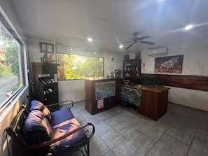 A room with a desk, chairs, a ceiling fan, a window with a view, and framed pictures on the wall. - Hotel Las Tres Banderas (Quepos)