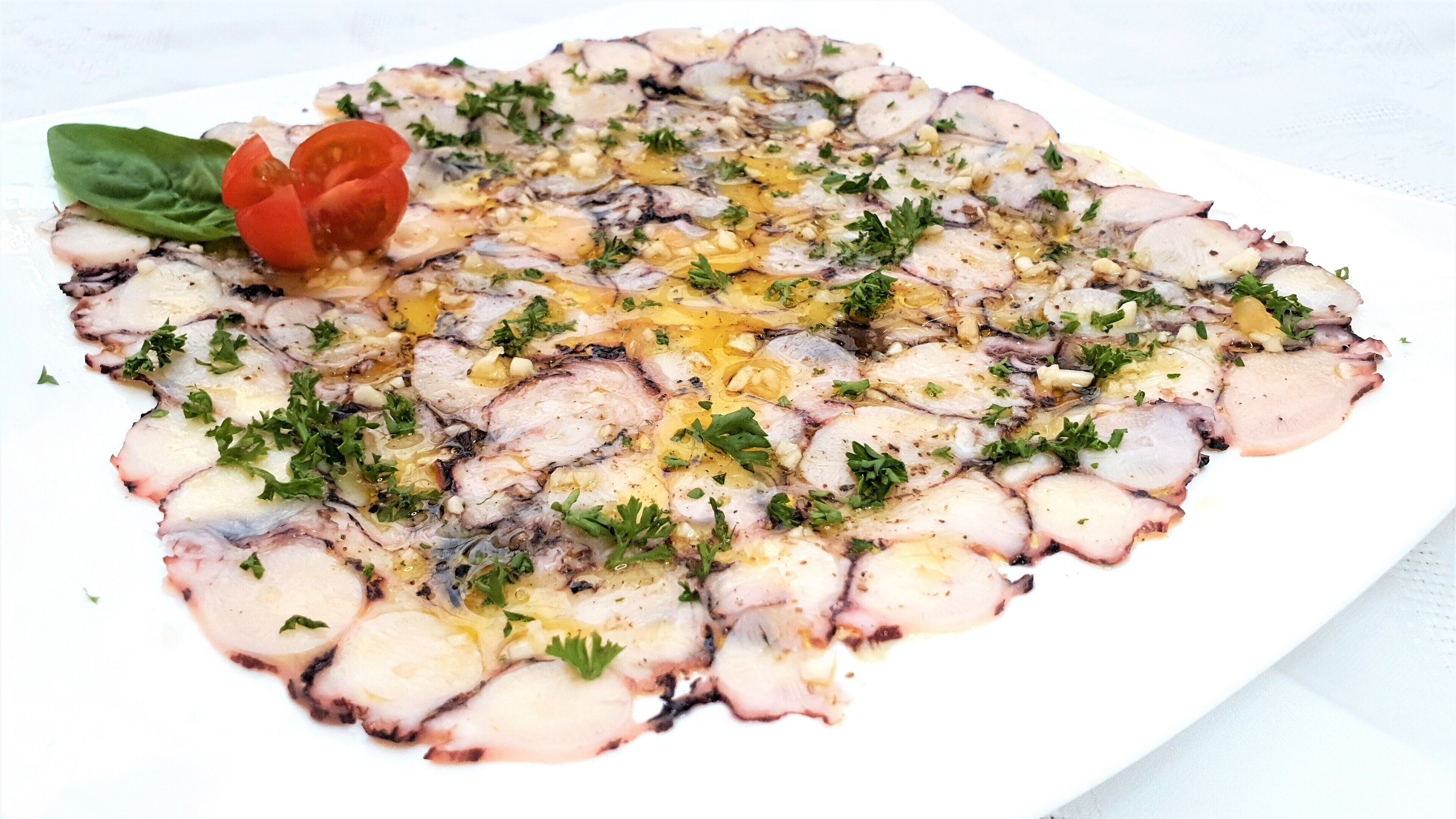 Un plato blanco con ensalada de pulpo, adornado con perejil y un tomate cherry.
