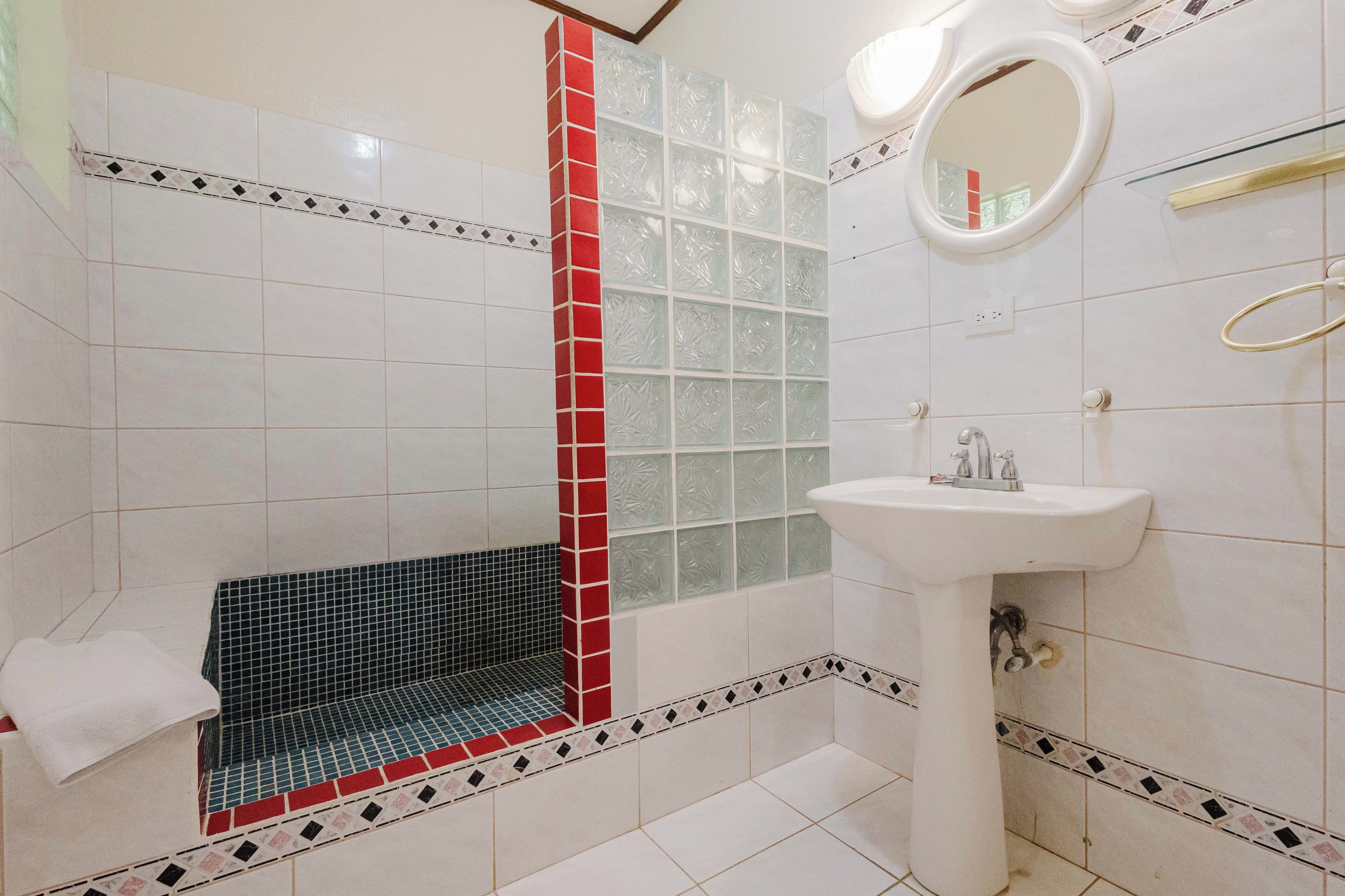 A bathroom with a white sink, a mirror, and a shower area with red and black tiles.