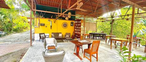 A covered outdoor seating area with wicker furniture, a dartboard, and a bookshelf.