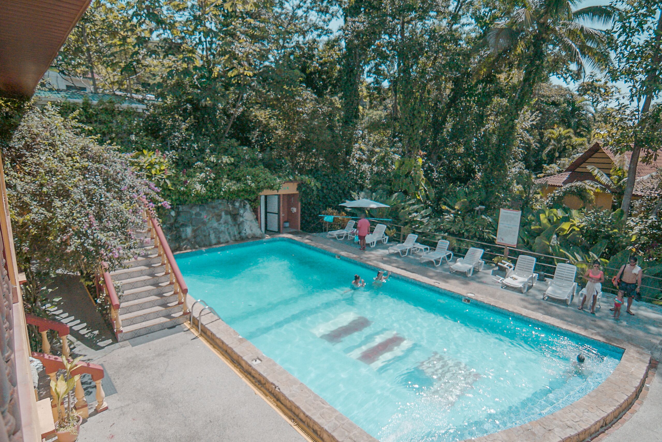 Piscina com degraus que levam a ela, cercada por árvores e um pequeno edifício.