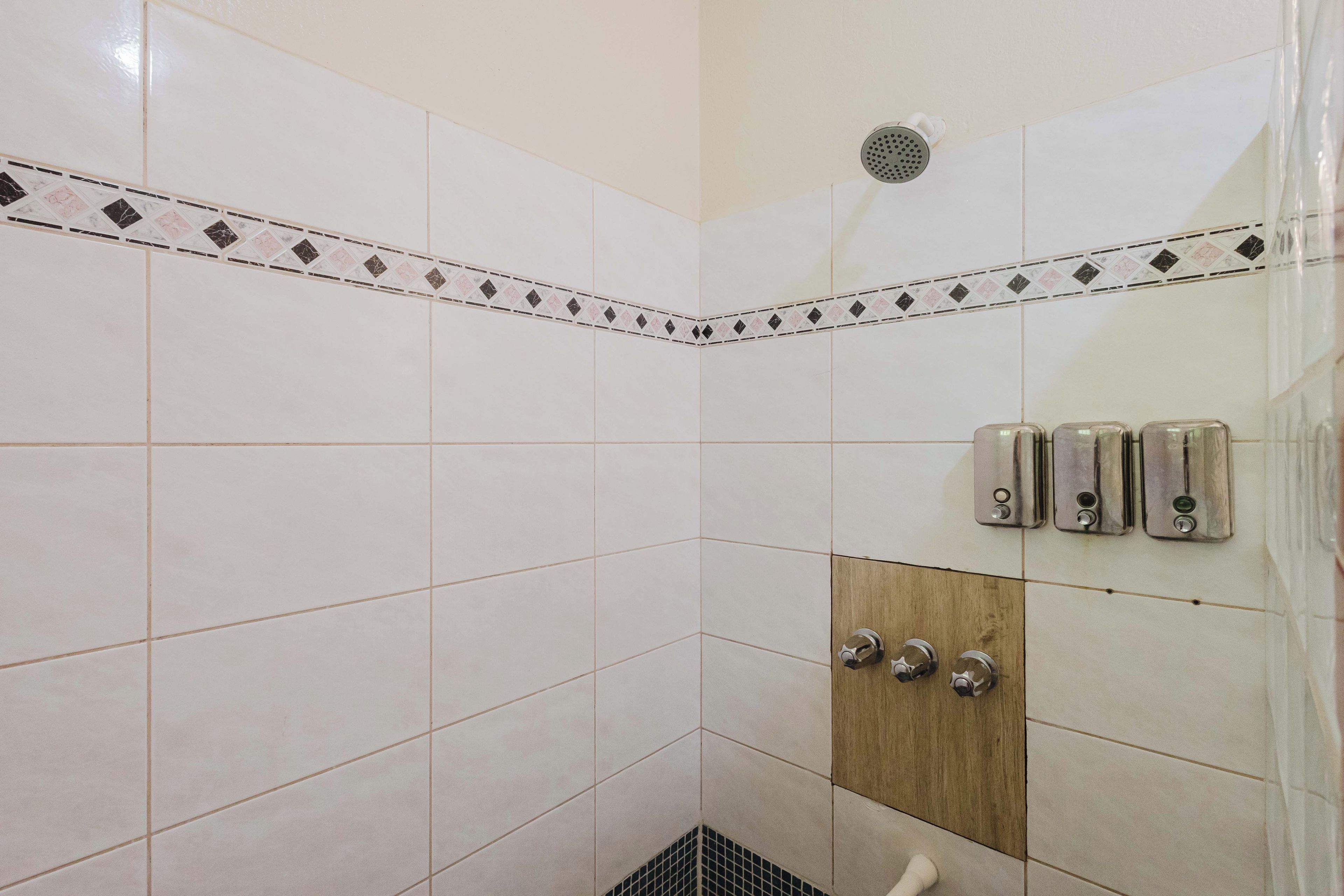A shower area with white tiles, a wooden panel, and a showerhead.
