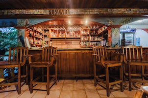 Zona de bar con sillas de madera, estantes llenos de botellas y un cartel que dice 'PURA VIDA'.