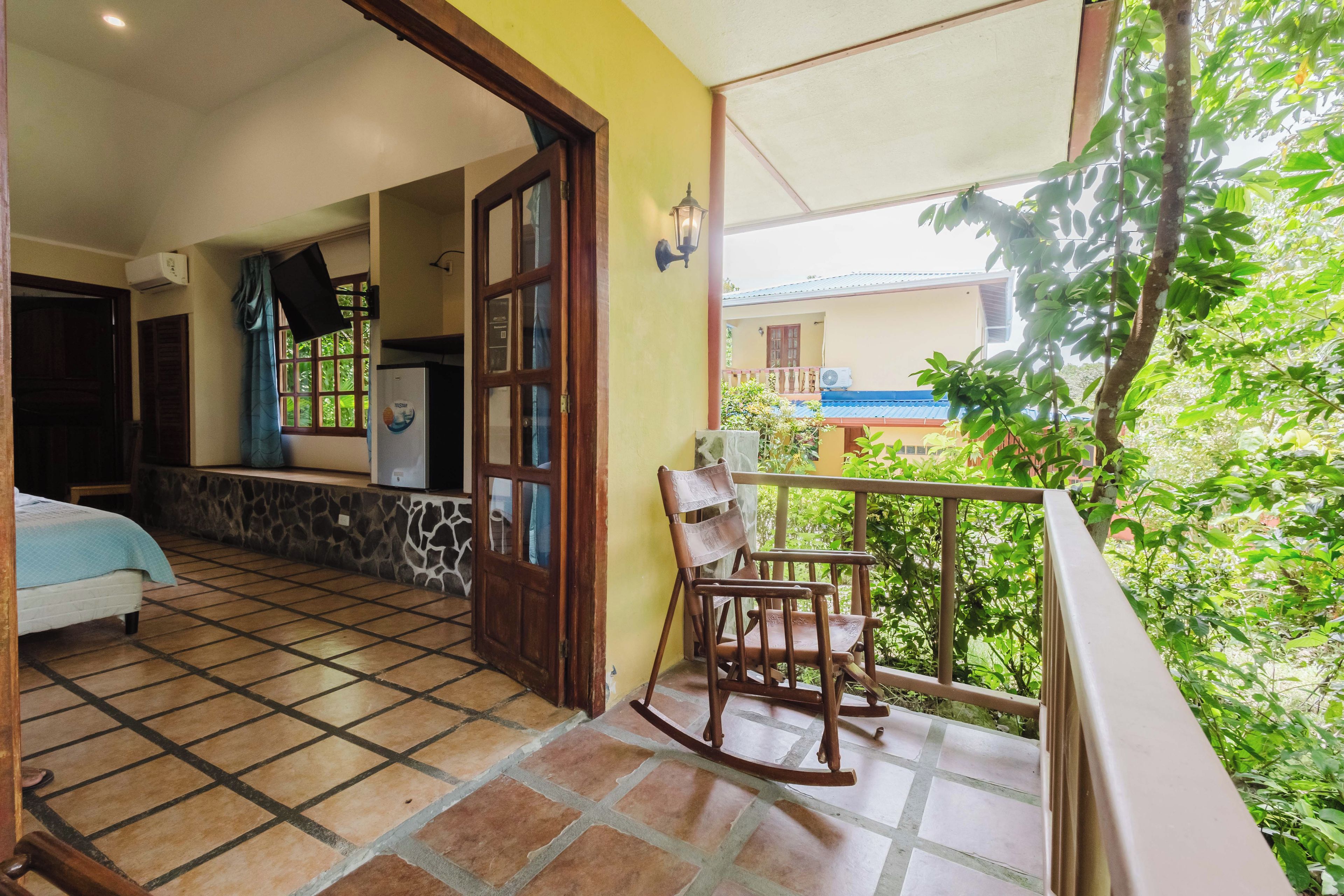 A room with a bed, a wooden door, a window, and a balcony with a chair.