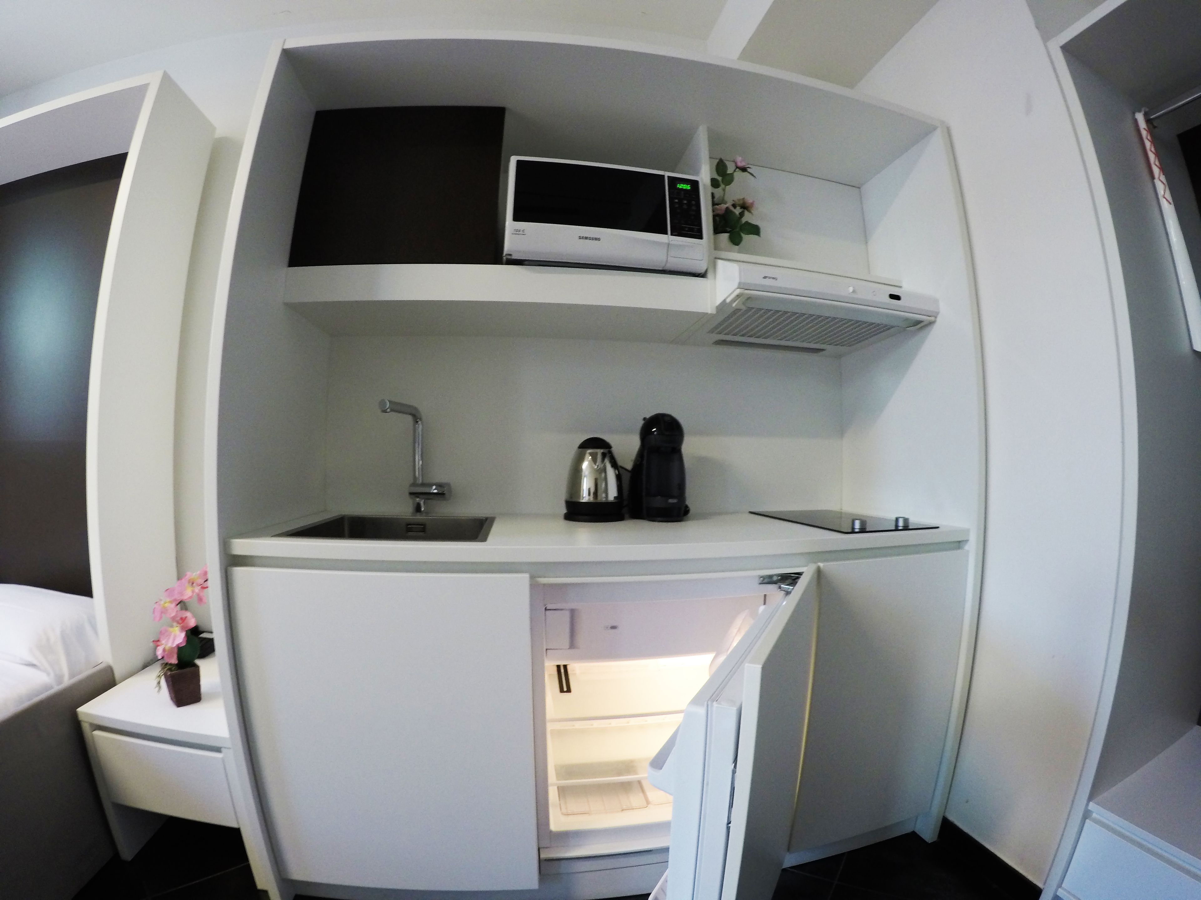 Una cucina compatta con forno a microonde integrato, macchina del caffè e lavello.