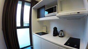 Una kitchenette compacta con microondas, cafetera y lavamanos.