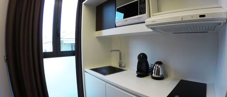 Una kitchenette compacta con microondas, cafetera y lavamanos.