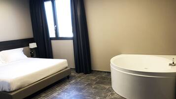 A hotel room with a bed, a large bathtub, and a window with curtains.