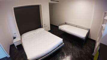 Hotelkamer met een groot bed, een kleiner bed, een nachtkastje, een stopcontact en een luchtbeheersingsunit aan de muur.