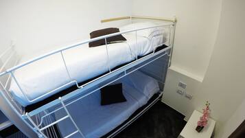 A bunk bed with a lower bunk, a small bedside table with a vase of flowers, and a power outlet on the wall.