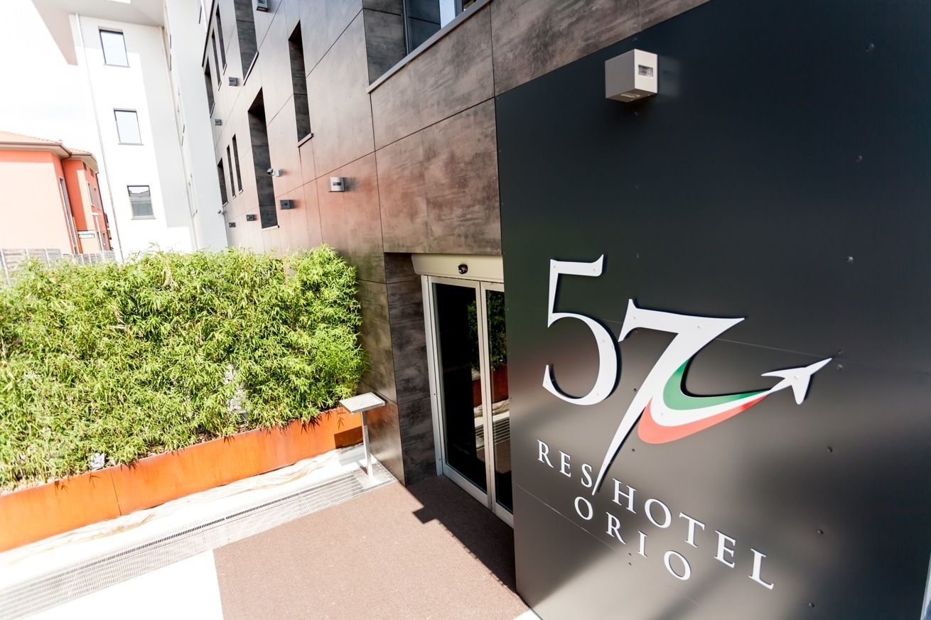 A modern hotel entrance with a large sign displaying the number 57 and the name "RENHOTEL ORIO".