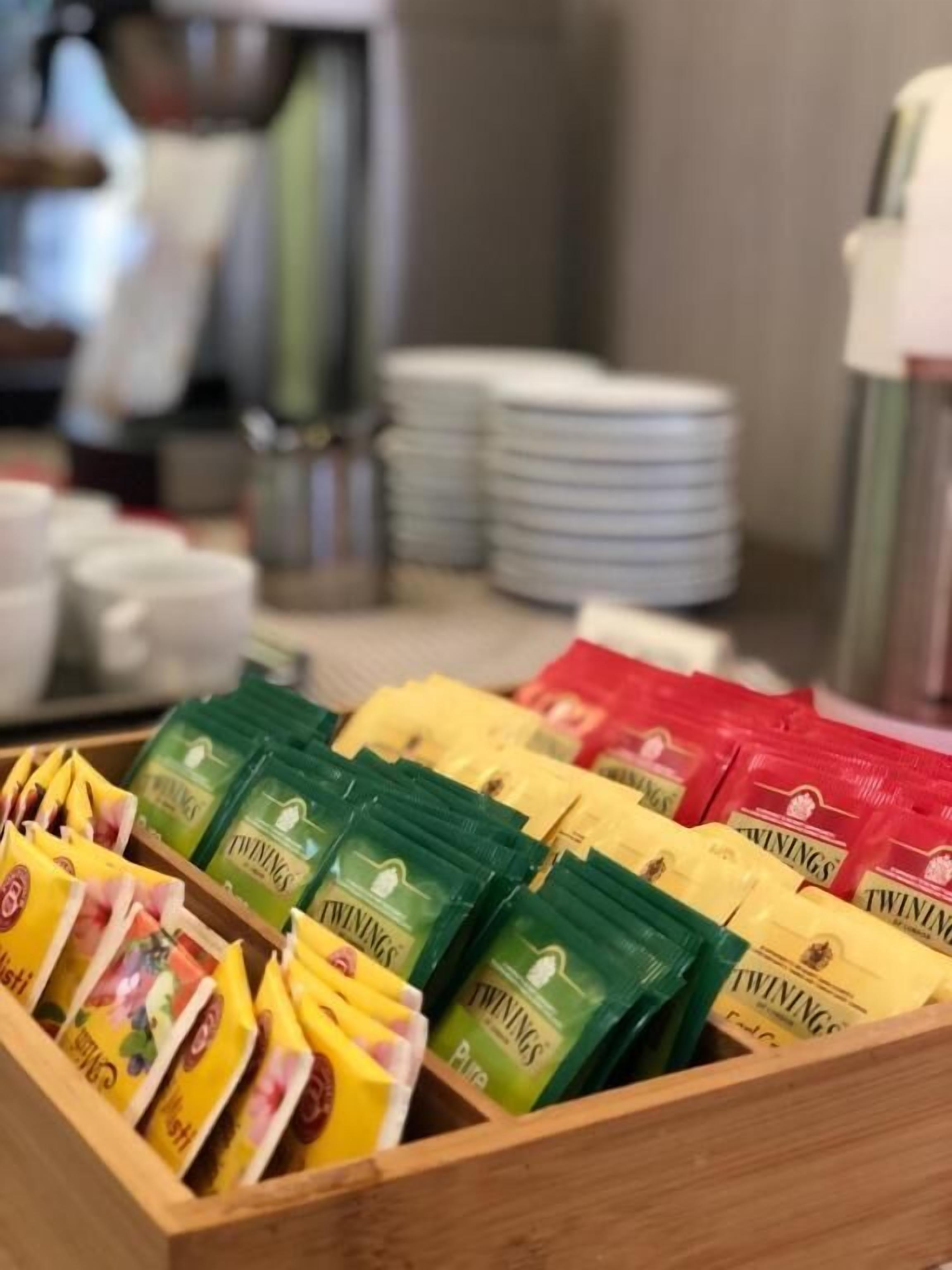 A wooden display case with Twinings tea packets in green, yellow, and red packaging.