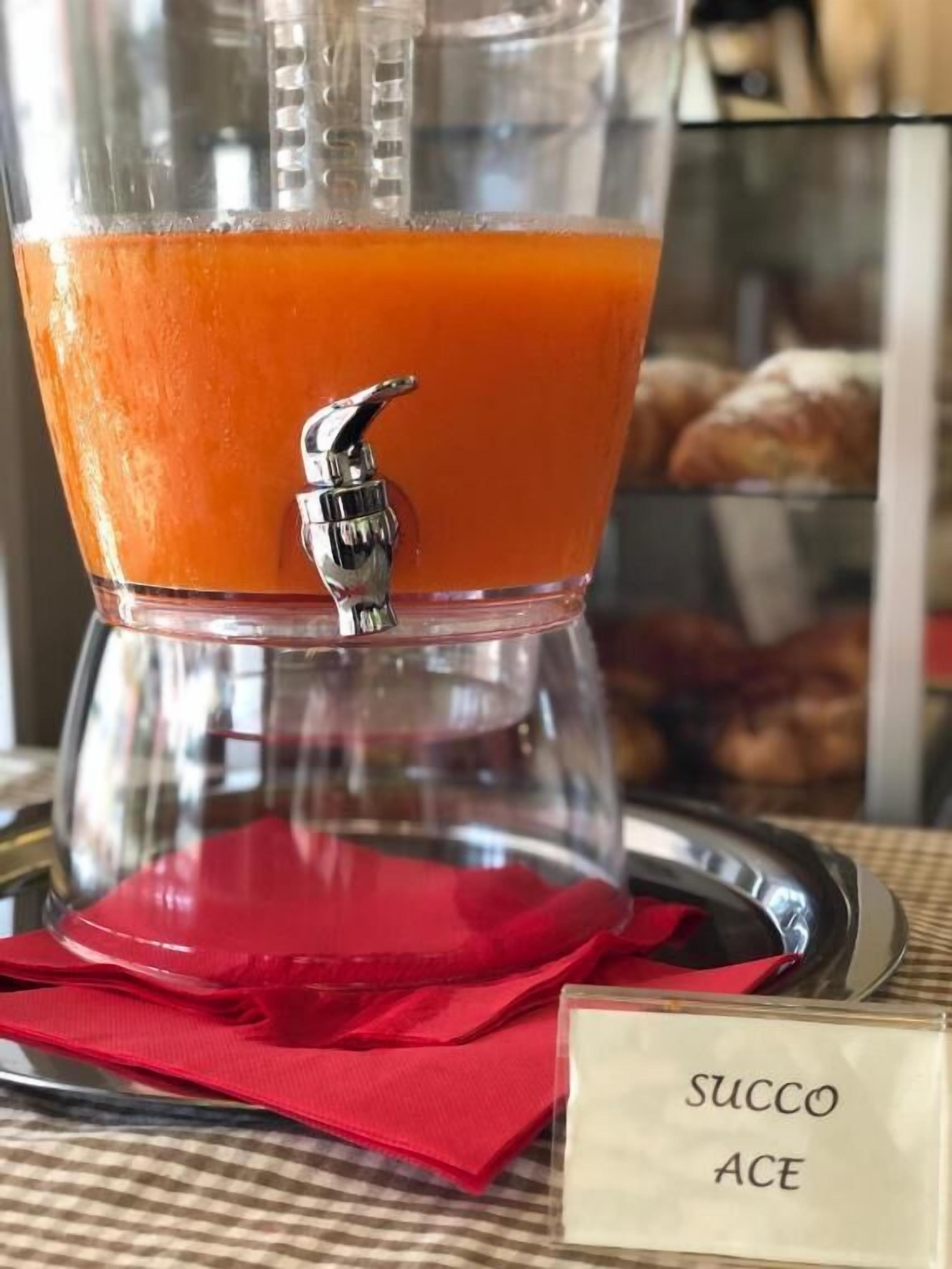 Un distributeur de jus avec une étiquette indiquant « SUCCO ACE », posé sur un plateau avec une serviette rouge.