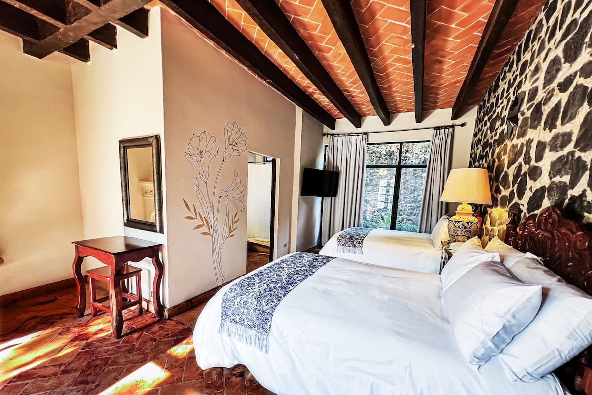 Um quarto com cama, escrivaninha, cadeira, espelho e janela com cortinas.