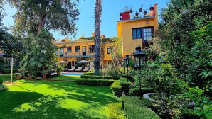 A well-maintained garden with a pool, neatly trimmed hedges, and a building with balconies. - Hacienda de las Flores (San Miguel de Allende)
