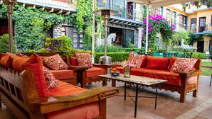 An outdoor seating area with wooden furniture and cushions, surrounded by lush greenery and a stone wall. - Hacienda de las Flores (San Miguel de Allende)