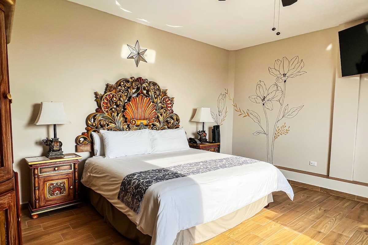 Quarto com uma cama grande, mesas de cabeceira de madeira, um painel de cabeceira decorativo, uma TV na parede e um adesivo floral.