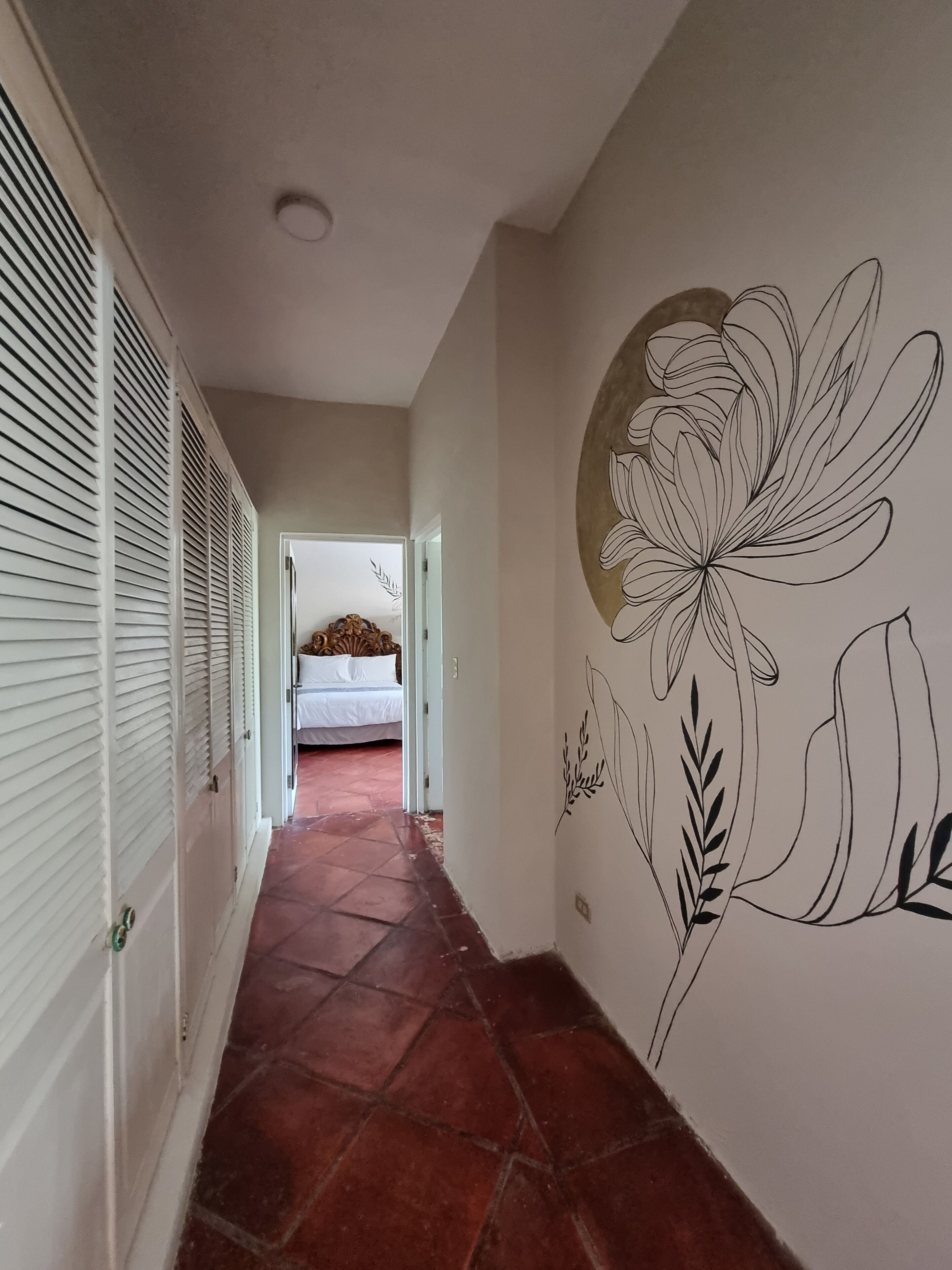 A hallway with a tiled floor, a bed in the background, and a wall with a floral mural.