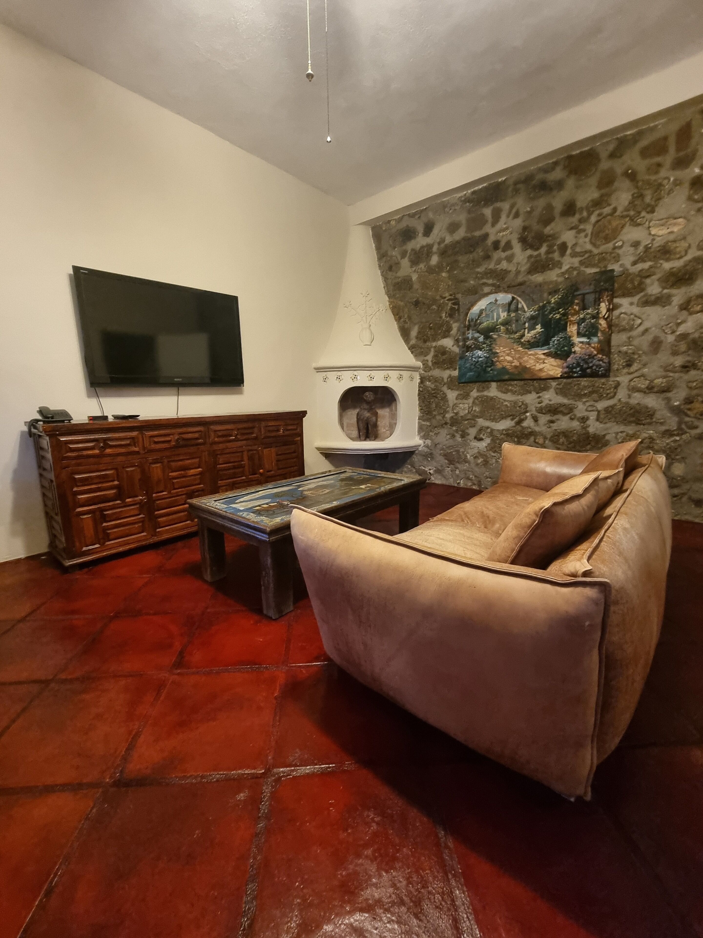 Un salón con sofá, una mesa de centro, televisor, chimenea y una pared de piedra con un cuadro.
