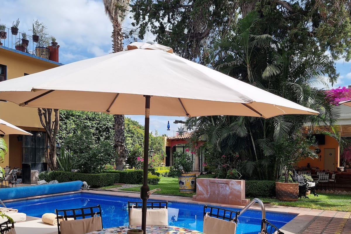 Uma área à beira da piscina com mesa, cadeiras e guarda-sol azulejados.
