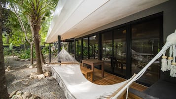 A hammock and wooden bench in a covered outdoor area with a view of the surrounding garden.