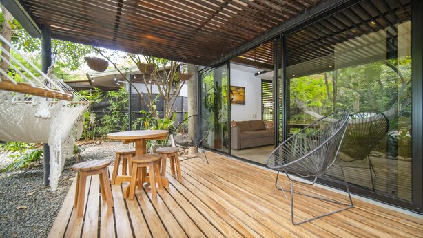 A wooden deck with outdoor furniture, a hammock, and a glass wall offering a view of greenery. - Las Avellanas Villas (Tamarindo)