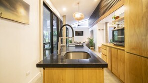 A modern kitchen with a central island, stainless steel sink, wooden cabinets, and a large window. - Las Avellanas Villas (Tamarindo)