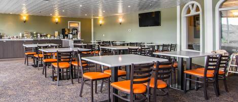 A restaurant with multiple tables and chairs, a counter with a beverage station, and a large window.