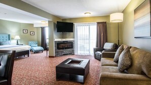 A hotel room with a bed, a sofa, a coffee table, a TV, and a fireplace. - Quality Hotel Drumheller (Drumheller)
