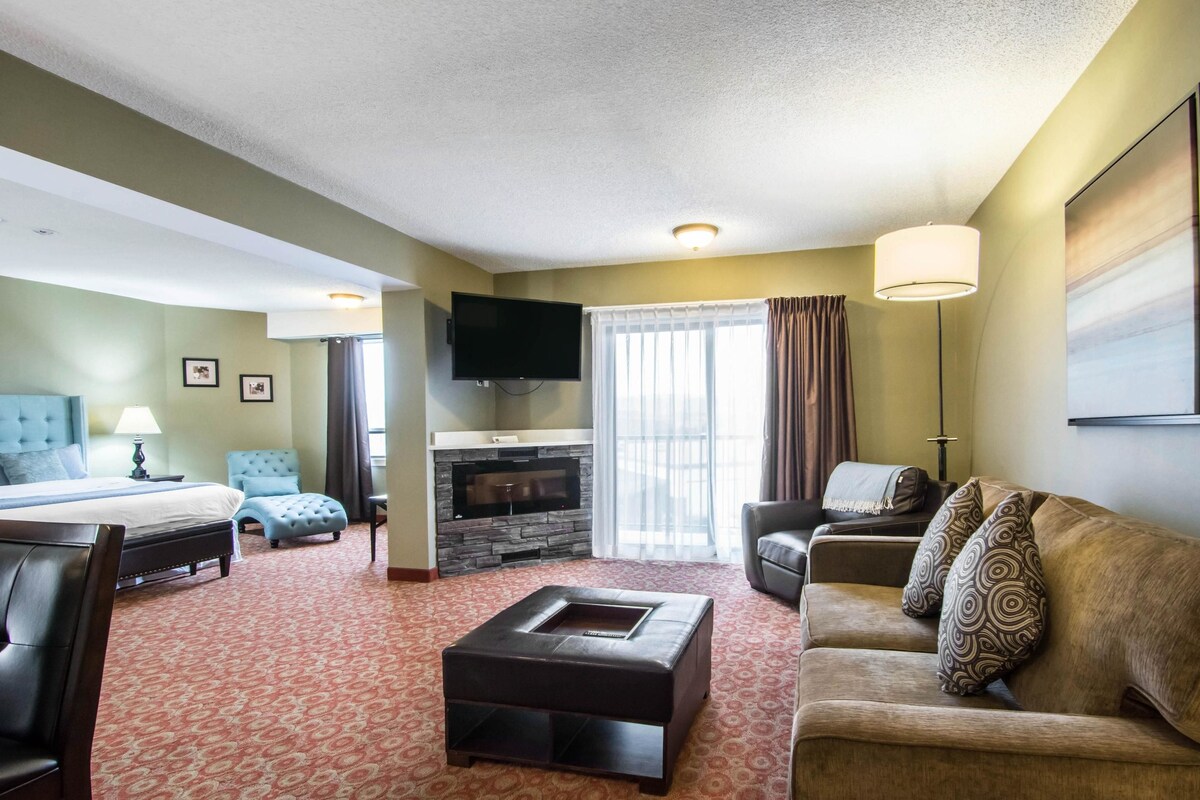 A hotel room with a bed, a sofa, a coffee table, a TV, and a fireplace.