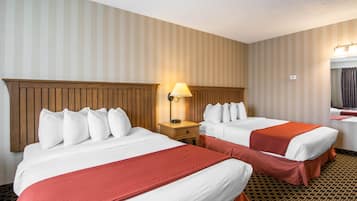A hotel room with two beds, wooden headboards, a nightstand with a lamp, and striped wallpaper.