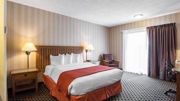 A hotel room with a large bed, two bedside tables with lamps, a chair, a desk, and a window with curtains.