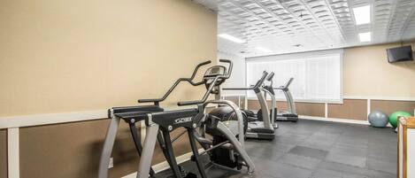 A gym with treadmills, exercise balls, and a TV mounted on the wall.