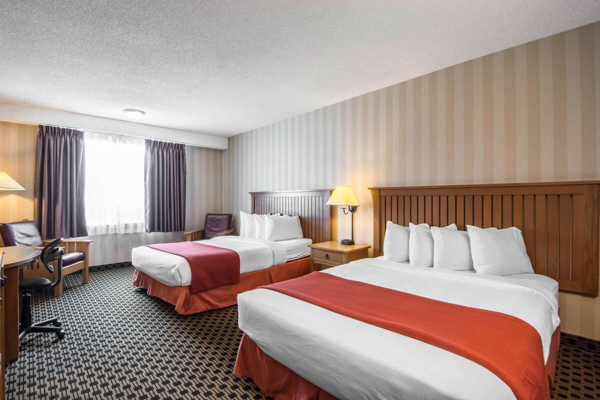 A hotel room with two beds, a desk, a chair, and a lamp.