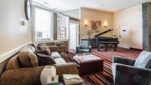 A hotel living room with a sofa, armchairs, a coffee table, a piano, and a fireplace. - Quality Hotel Drumheller (Drumheller)