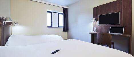 Habitación de hotel con una cama grande, un escritorio con una computadora portátil, un televisor montado en la pared y una ventana con cortinas.