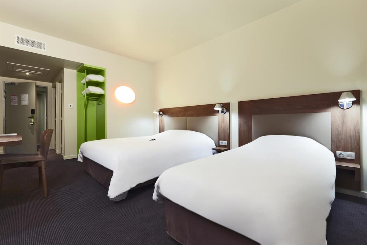 A hotel room with two beds, a desk, and a chair.