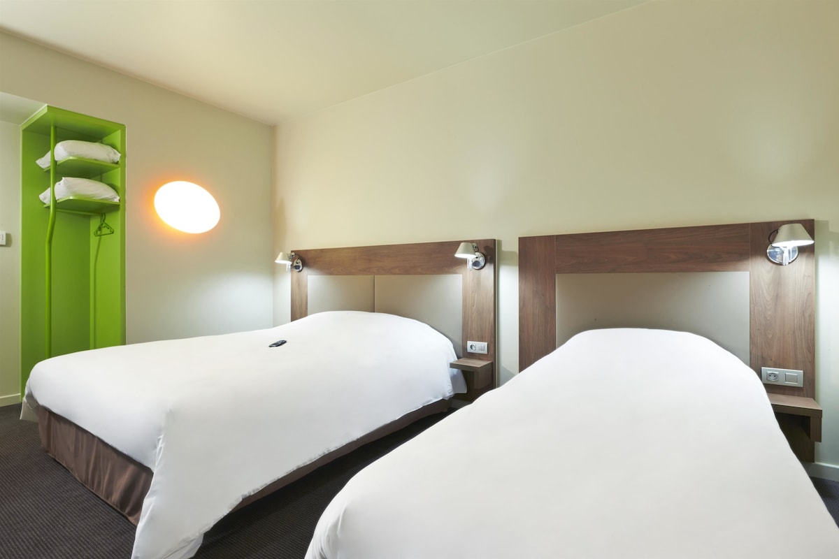 A hotel room with two single beds, a green wardrobe, and a round wall light.