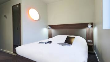 Une chambre d’hôtel équipée d’un lit, d’un ordinateur portable, d’une lampe de chevet et d’une applique murale.