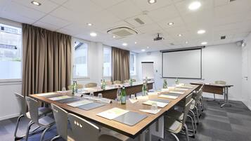 Una sala conferenze con un lungo tavolo, sedie, uno schermo per proiettore e una lavagna.