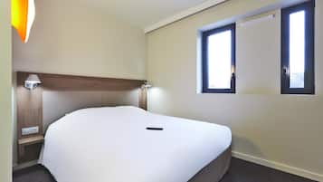 Una cama bien hecha en una habitación de hotel, con cabecera, mesita de noche, lámpara y ventana.