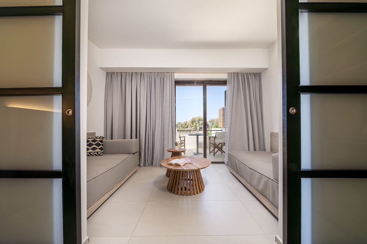 Uma sala de estar moderna com uma mesa redonda de madeira, dois sofás e vista para o exterior através de grandes janelas.