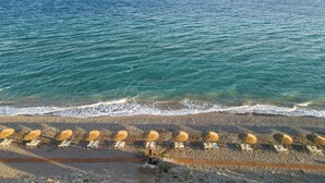 A beach with rows of sun loungers and umbrellas, a wooden boardwalk, and a view of the sea and distant mountains. - D'Andrea Mare Beach Hotel – All Inclusive (Rhodes)