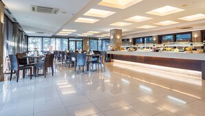 A modern hotel dining area with a central buffet, large windows, and a clean, tiled floor. - D'Andrea Mare Beach Hotel – All Inclusive (Rhodes)