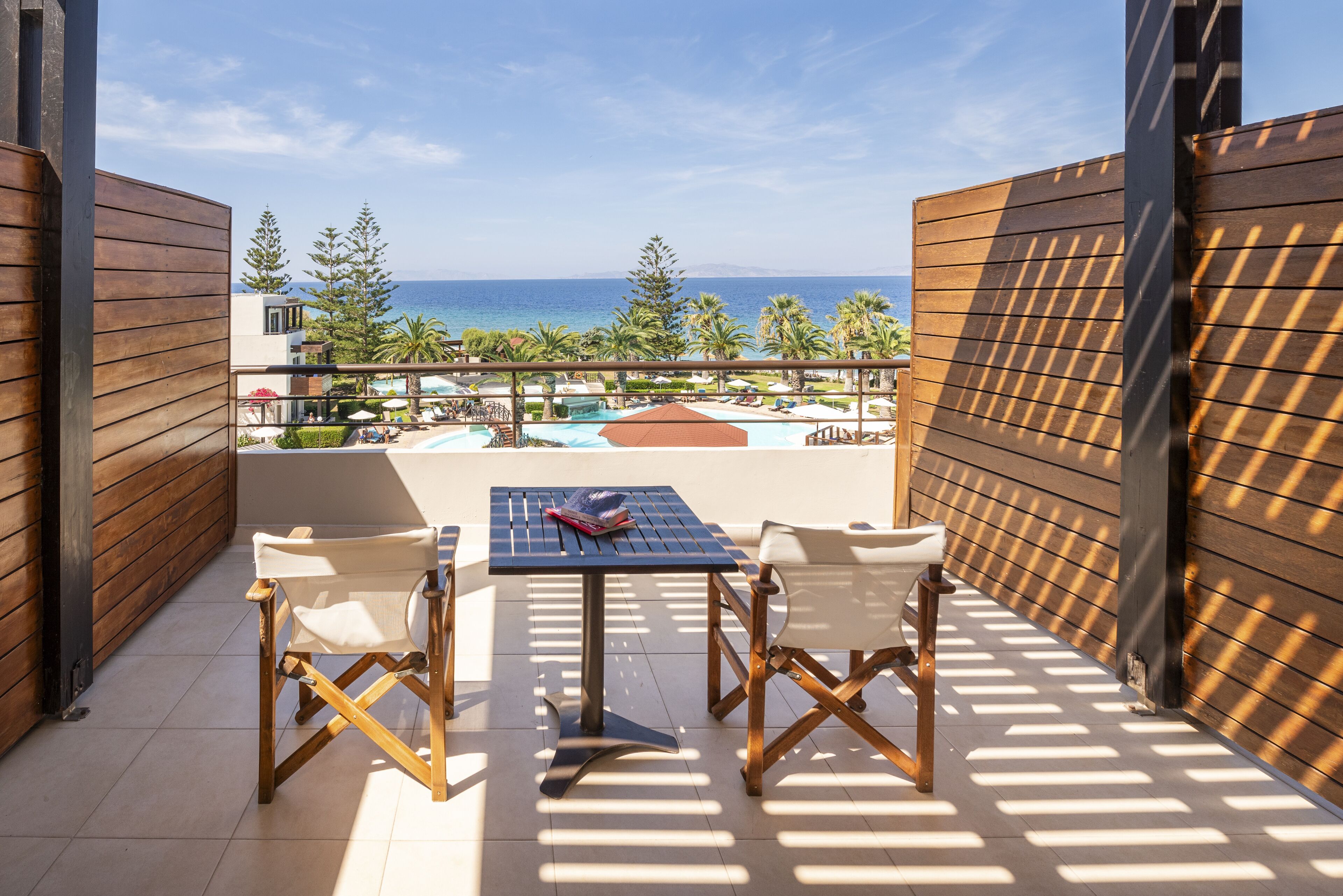 A balcony with a table and chairs, overlooking a pool and a view of the ocean.