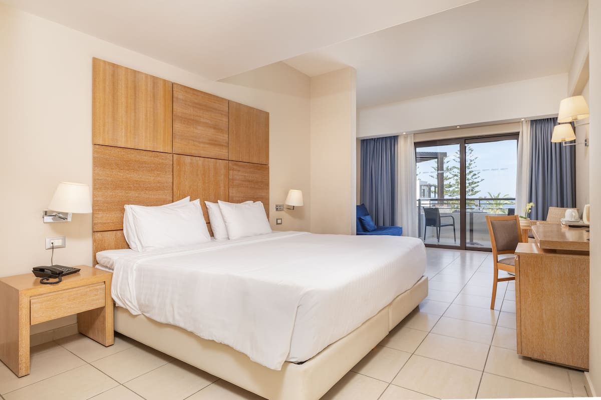 Quarto de hotel com cama grande, escrivaninha e varanda com vista.