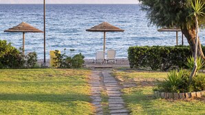 A pathway leading to beachside seating with umbrellas, a grassy area, and a view of the sea. - D'Andrea Mare Beach Hotel – All Inclusive (Rhodes)